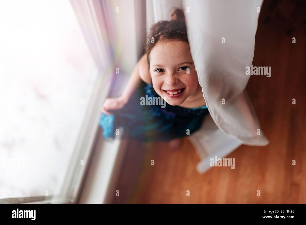 Portrait d'une jeune fille debout près d'une fenêtre tenant le rideau Banque D'Images