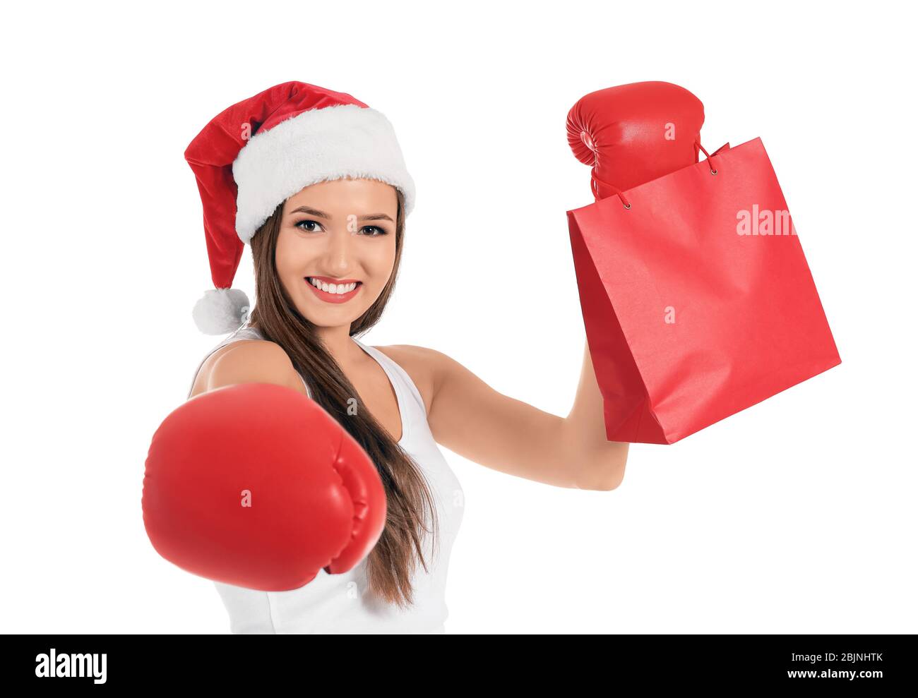 Belle jeune femme dans le chapeau du Père Noël avec gants de boxe et sac de shopping sur fond blanc. Concept du Boxing Day Banque D'Images