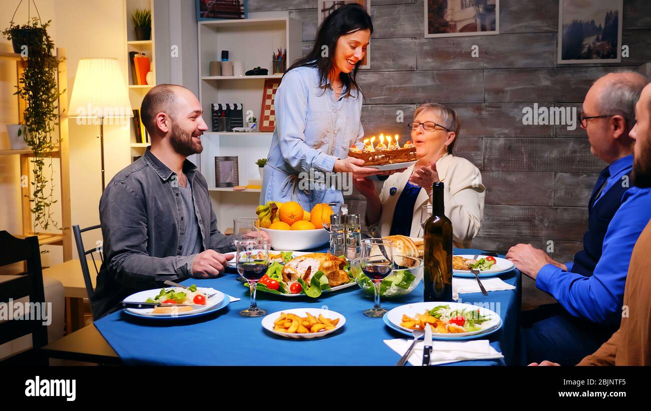 Suivez le cliché de la femme avec un gâteau d'anniversaire pour son mari au dîner en famille. Banque D'Images