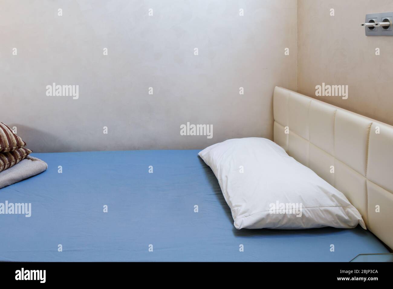 Le lit simple est recouvert d'une feuille bleue. Sur le lit est un oreiller blanc doux. Banque D'Images