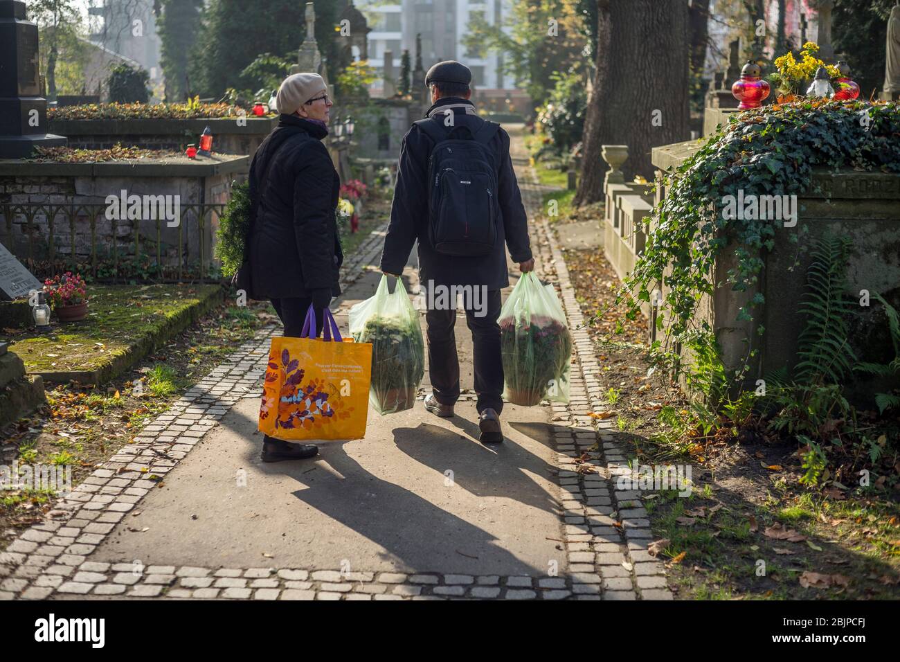 Un couple promenades remplies de sacs en plastique avec des fleurs sur le cimetière de Rakowicki à Cracovie, Pologne 2019. Banque D'Images