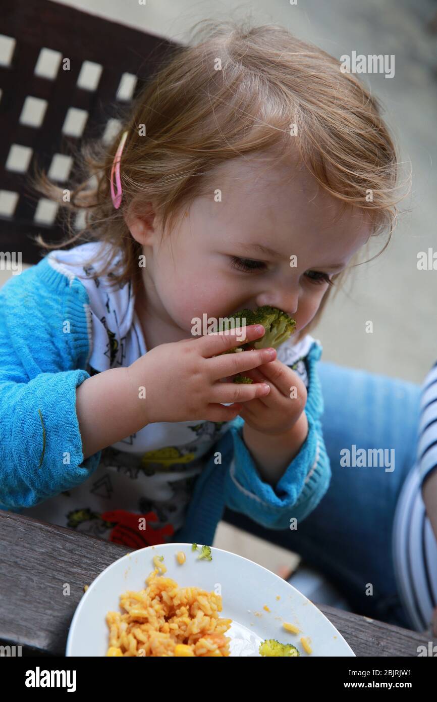 Une jeune fille mange des pâtes et du brocoli. Banque D'Images