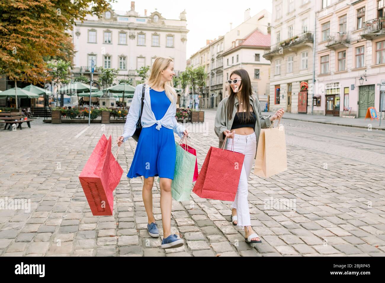Deux charmantes femmes caucasiennes, blonde et brune amis, tenant des sacs  d'achats, souriant joyeusement, parlant entre elles, tout en marchant dans  la vieille ville Photo Stock - Alamy