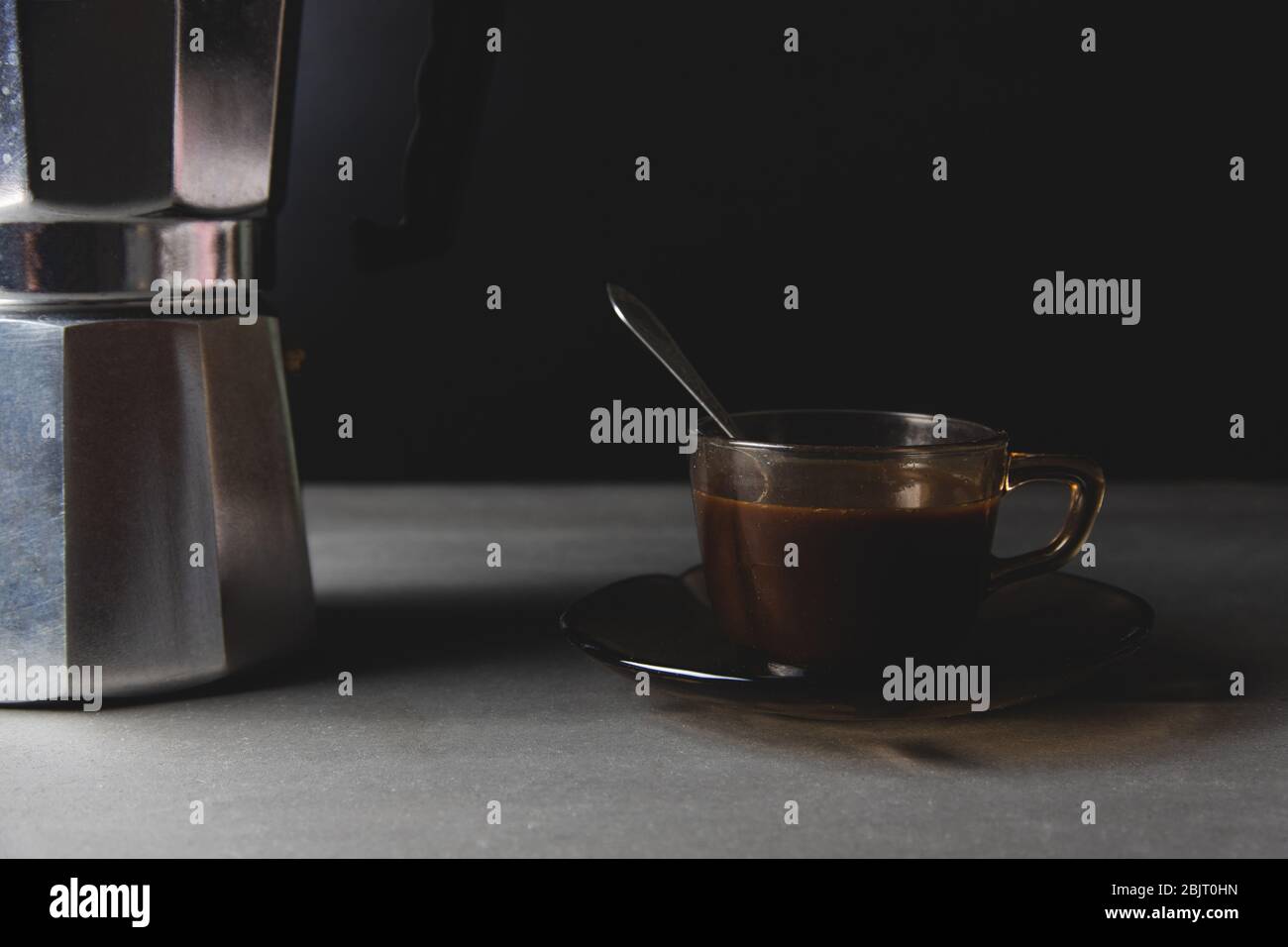 Vue horizontale sur un verre brun de café et une cafetière italienne, sur fond noir Banque D'Images