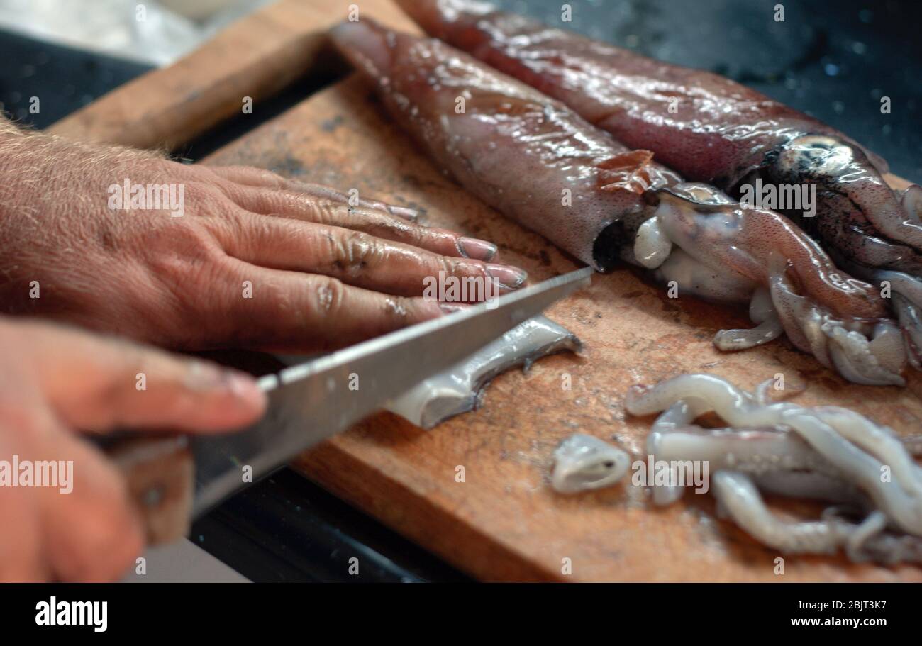 L'homme a coupé et tiré le cartilage dans Calamari. La planche à découper de peinture à l'encre de calmar et la main de l'homme Banque D'Images