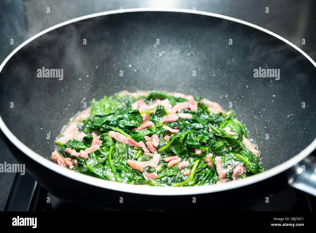 Cuisson des épinards avec du bacon en dés dans un wok antiadhésif Banque D'Images
