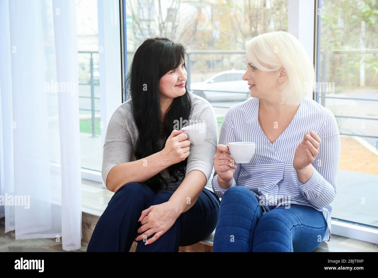 Les femmes matures séduisantes boivent du café près de la fenêtre à la maison Banque D'Images