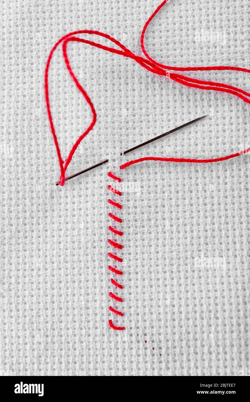 Points de broderie en fil rouge et aiguille à coudre sur tissu blanc Banque D'Images