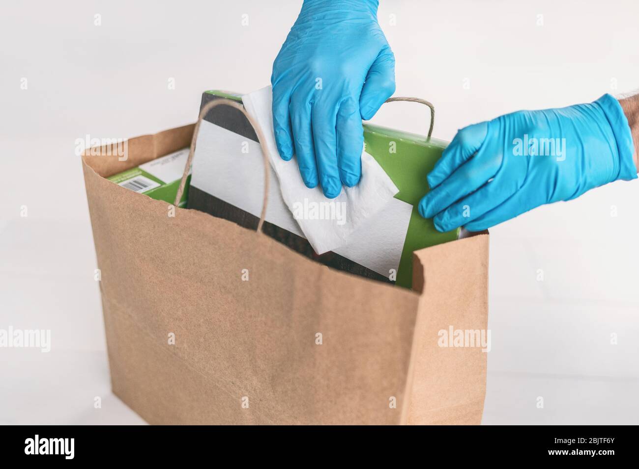 Désinfecter les surfaces des emballages du sac de livraison d'aliments avec des gants et des lingettes désinfectantes à la maison. COVID-19 hygiène préventive. Banque D'Images