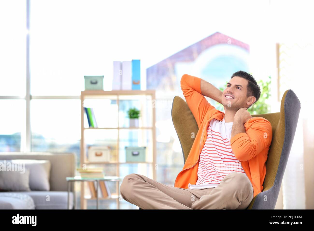 Beau jeune homme assis dans un fauteuil confortable à la maison Banque D'Images