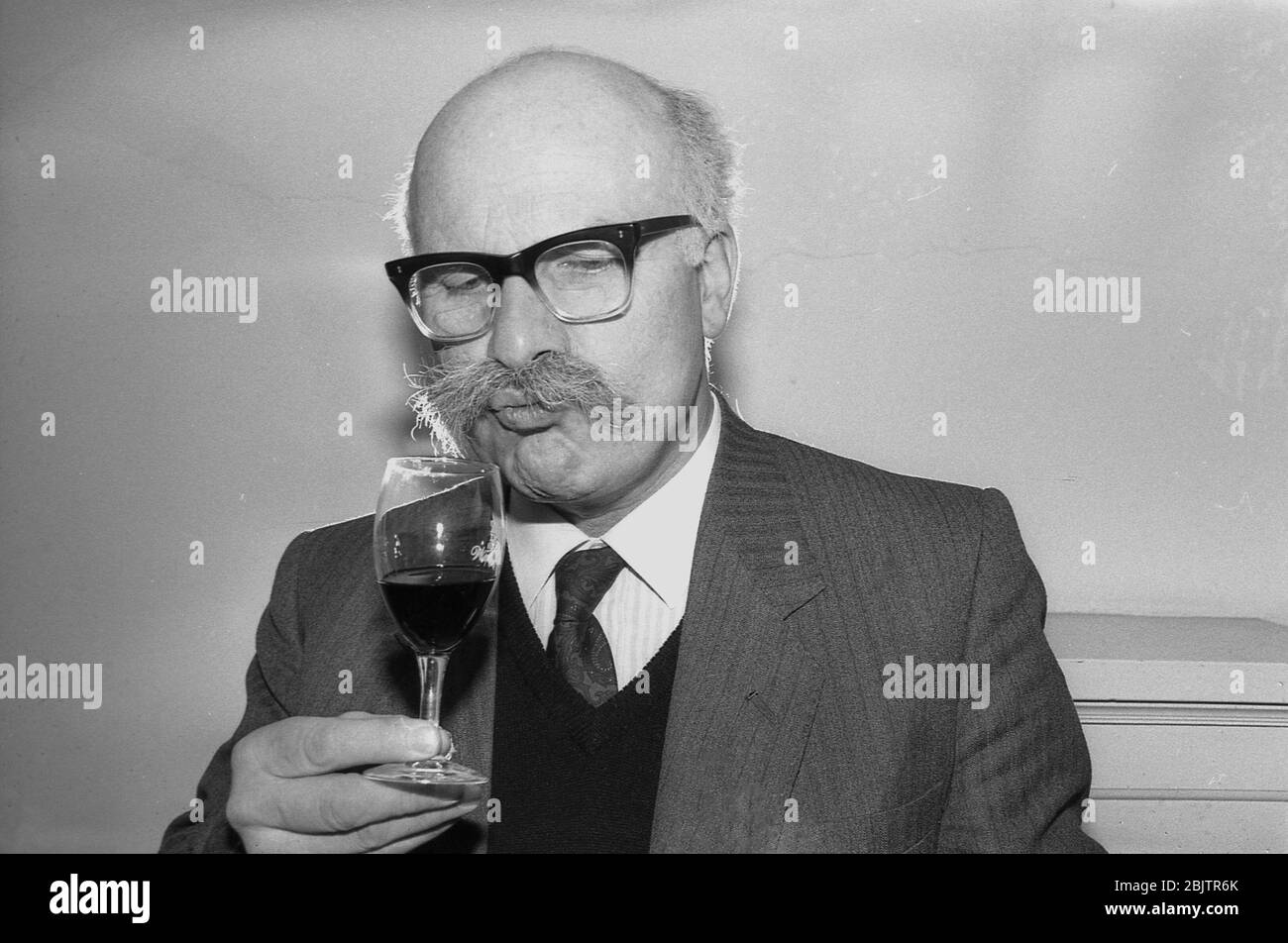 1980, historique, lors d'une dégustation de vins, un homme portant une veste et une cravate A et avec une moustache bushy qui ronfle un verre de vin rouge, pour sentir l'arôme, le bouquet du vin, Angleterre, Royaume-Uni. Banque D'Images