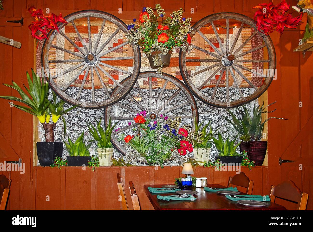 Traitement décoratif des fenêtres, éclectique, 3 roues de wagon, plantes en pots, fleurs artificielles, courtepointe, dentelle, table, restaurant, établissement de Patti dans les années 1880 Banque D'Images