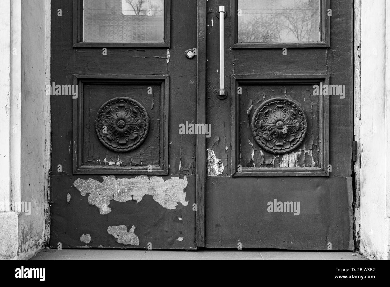 Photo en noir et blanc des éléments architecturaux de la vieille porte avec peinture écaillée et taches. Rosettes sculpturales en cadres carrés de panneaux de portes Banque D'Images