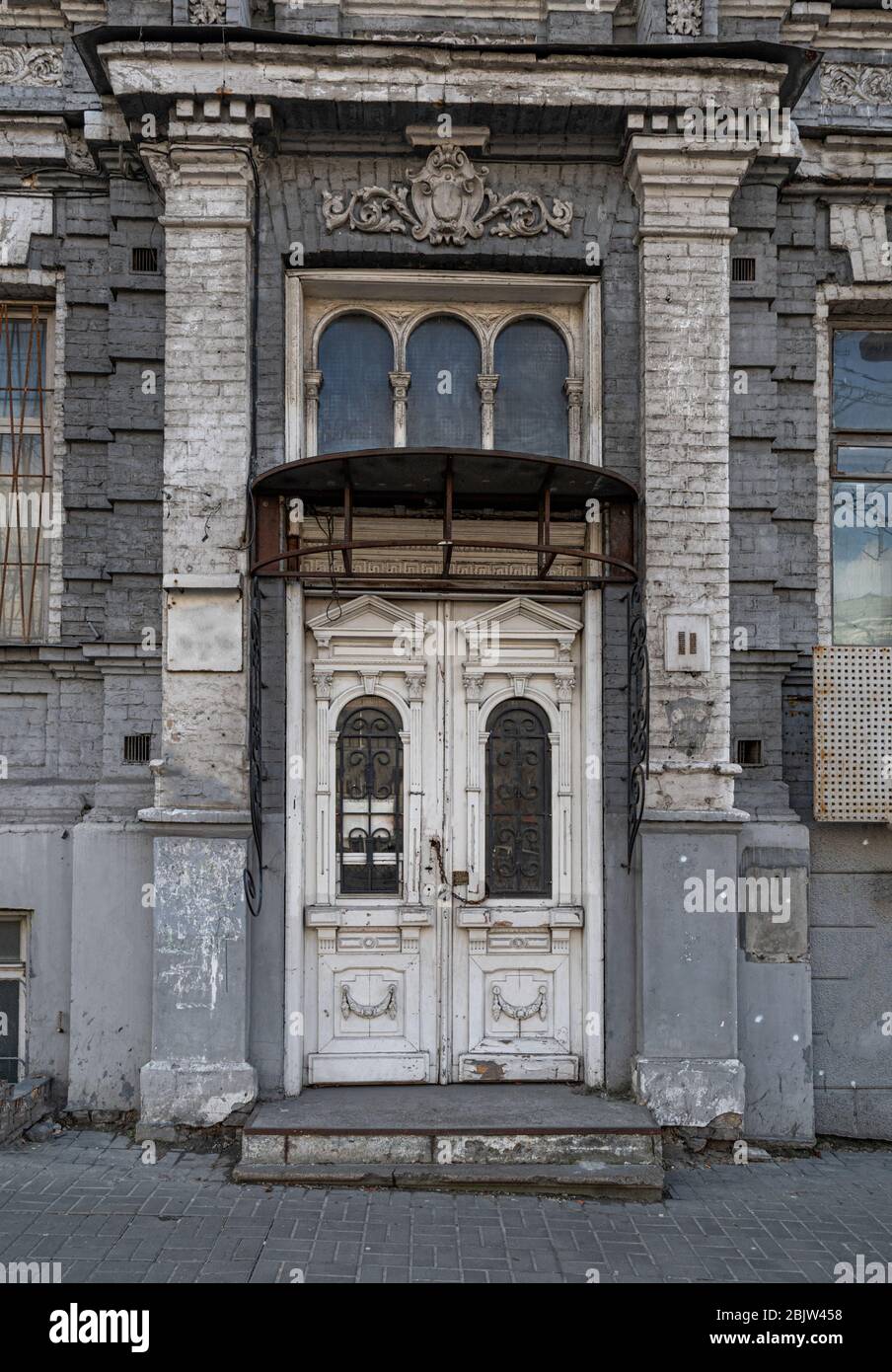 Façade de l'ancien bâtiment avec mur sale de briques et colonnes par les côtés de la porte blanche en bois chaînée par un cadenas. Architecture de la ville européenne. Rétro bu Banque D'Images