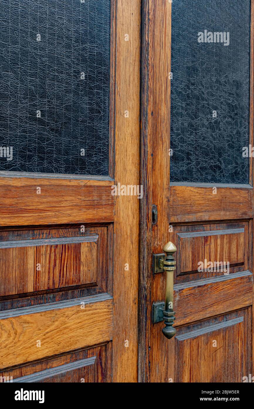 Panneaux de portes doubles en bois avec fenêtres rectangulaires et verre mat à motifs à l'intérieur des cadres. Poignée de porte en laiton métallique sur le grunge vieilli texture bois closeu Banque D'Images