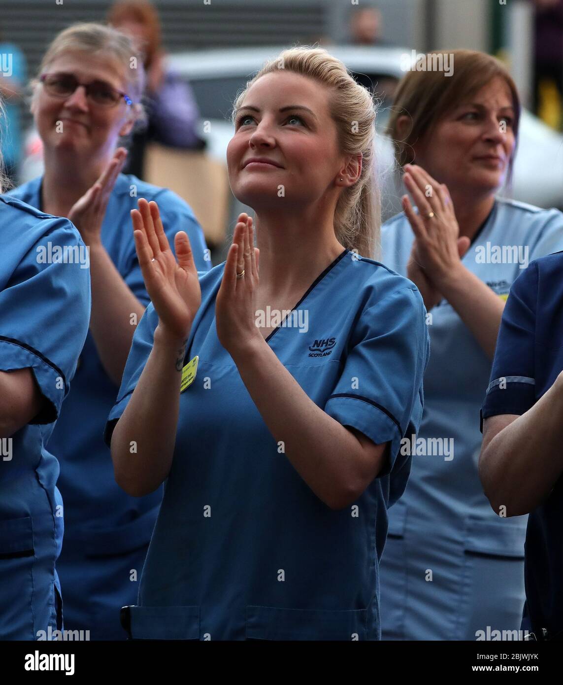 Les infirmières se sont accrochez à leurs collègues alors qu'elles regardent d'une fenêtre à l'hôpital universitaire Queen Elizabeth de Glasgow alors qu'elles se joignent aux applaudissements pour saluer les héros locaux au cours du Clap national de jeudi pour que les soignants reconnaissent et soutiennent les travailleurs et les soignants du NHS qui luttent contre la pandémie de coronavirus. Banque D'Images