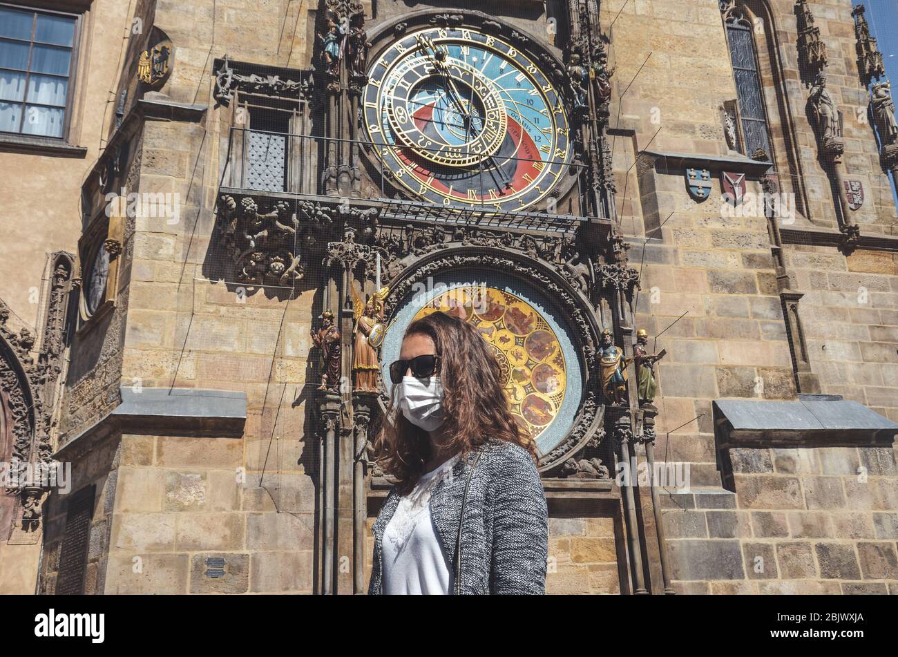 Jeune femme caucasienne avec lunettes de soleil et masque médical photographié devant l'horloge astronomique Orloj à Prague, en République tchèque. Voyager, tourisme pendant coronavirus. Concept COVID-19. Banque D'Images
