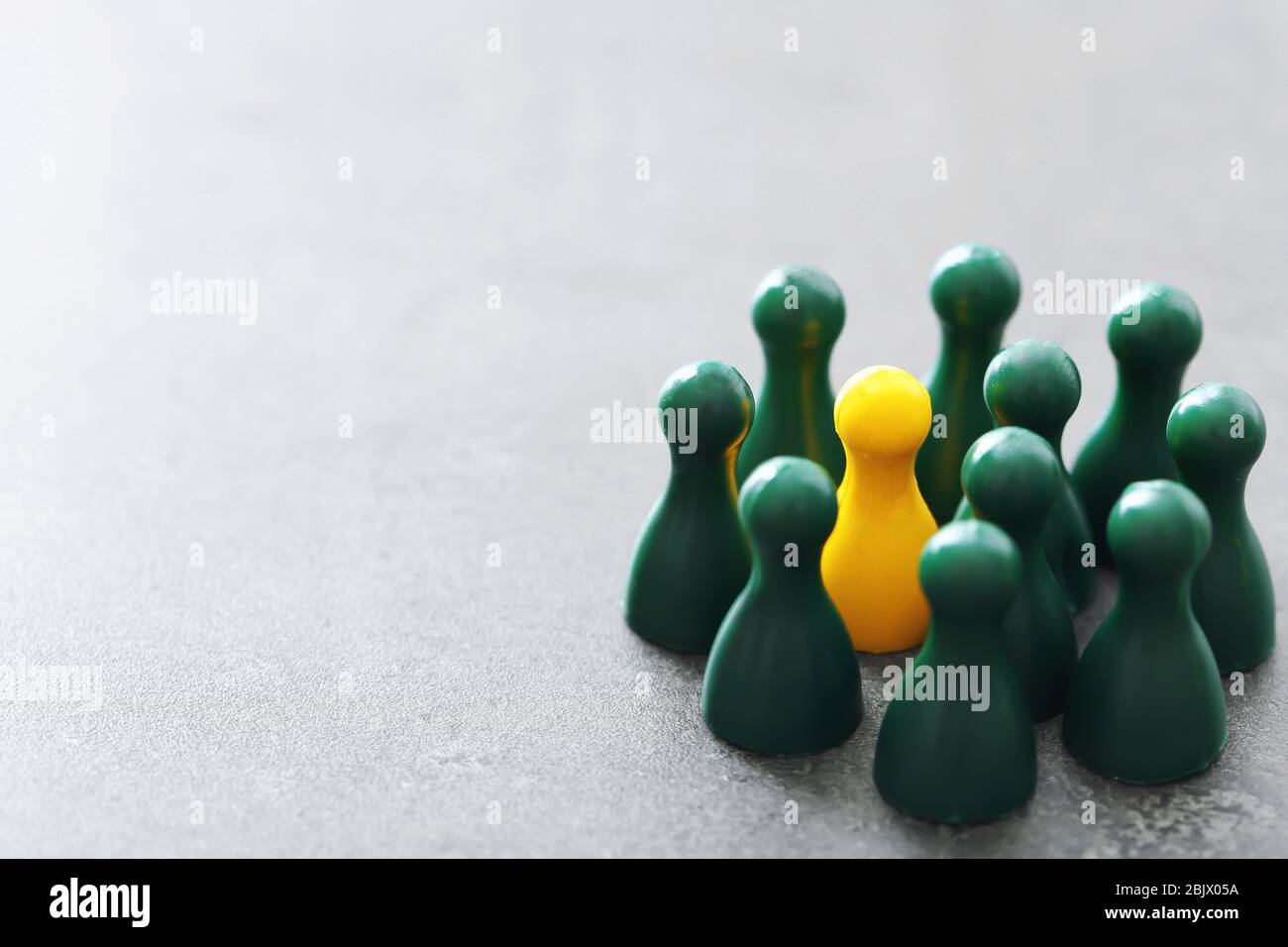 Pion jaune parmi les pions verts sur la table grise. Concept de différence et d'unicité Banque D'Images