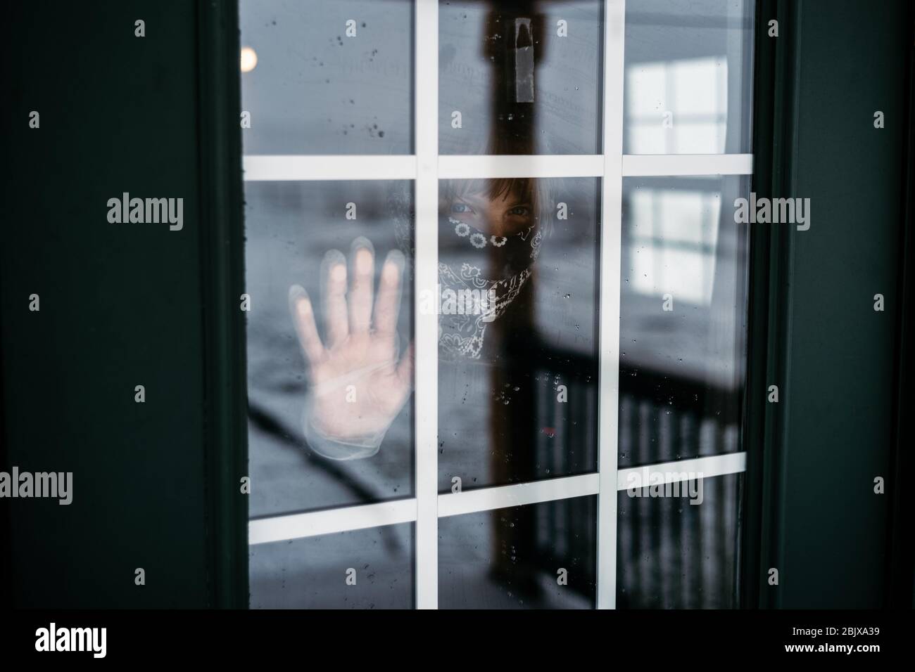 Une triste femme portant un masque EPI et des gants à l'intérieur manque le monde extérieur pendant un séjour de pandémie covid-19 à la maison, se verrouiller. En regardant dans la fenêtre Banque D'Images