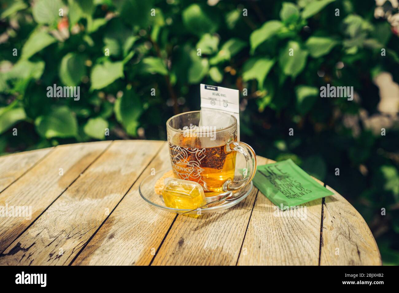 Thé sain à base de plantes en verre avec miel, biscuit à biscuits, cuillère à café, sucre. Table ronde en bois à l'extérieur dans l'arrière-cour. Thé vert sur le dos feuilles Banque D'Images