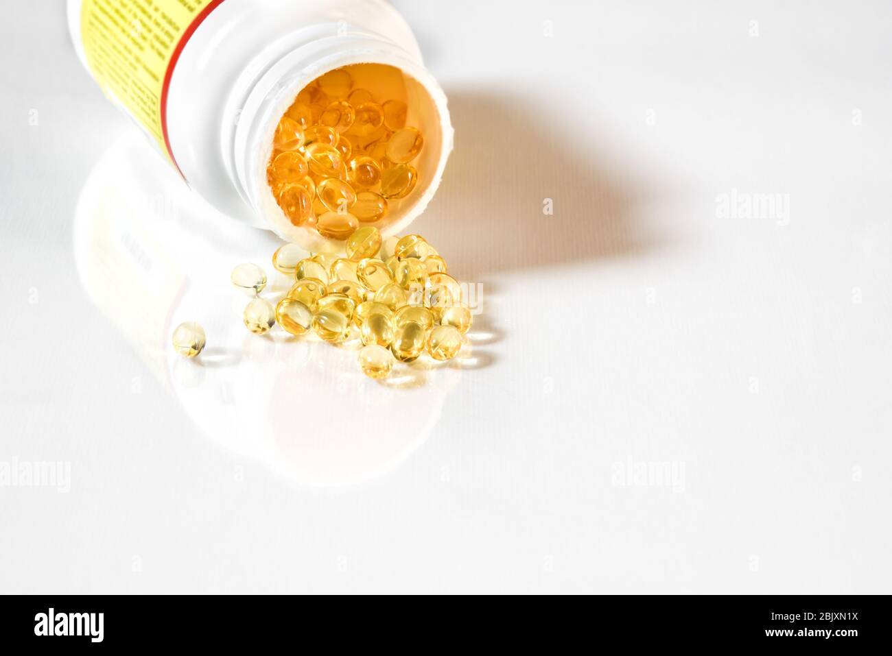 Capsules de gel jaune clair de vitamine D 3 qui débordent de la bouteille de complément. Fond blanc avec espace de réflexion et de copie Banque D'Images