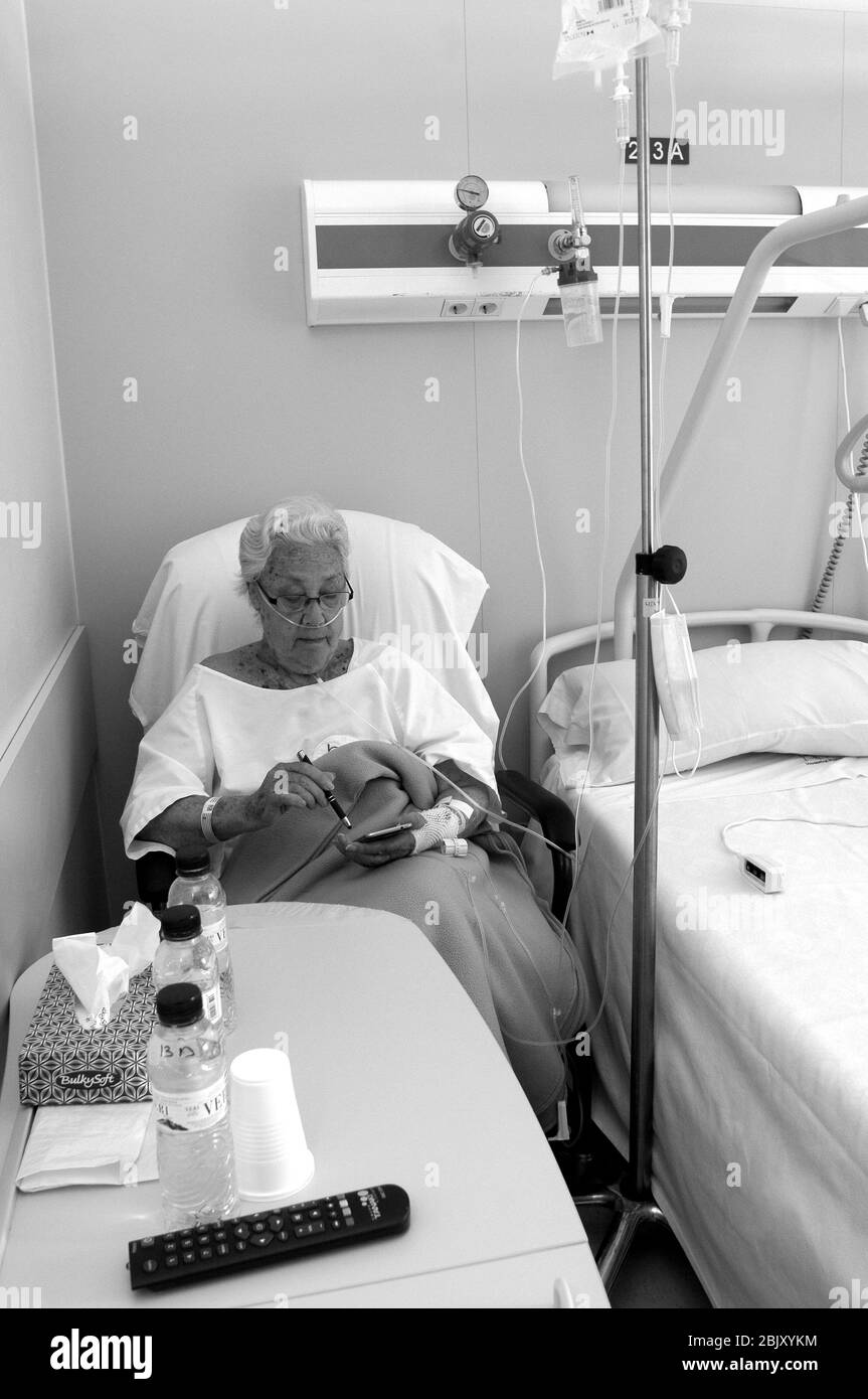 Femme assise par le lit, reliée à différents itinéraires aux médicaments intraveineux. À l'hôpital Plató de Barcelone Banque D'Images