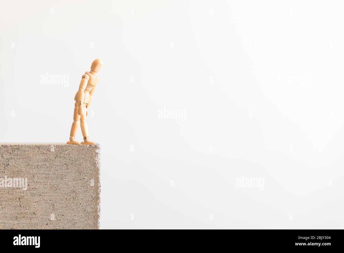 Figure humaine en bois debout sur le bord d'un bloc de béton, regardant vers le bas. Banque D'Images