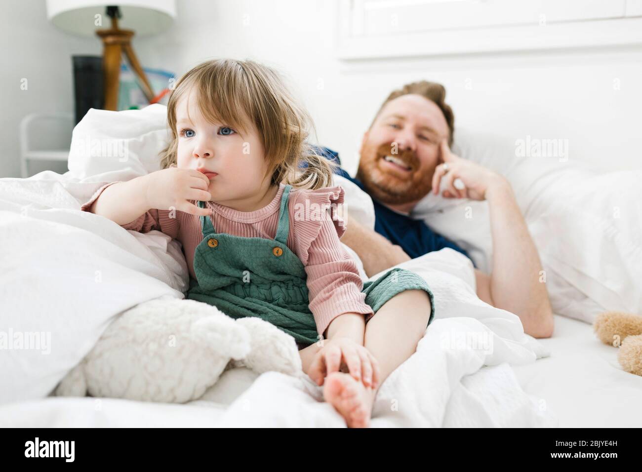 La fille (2-3) et le père regardant la télévision dans le lit Banque D'Images
