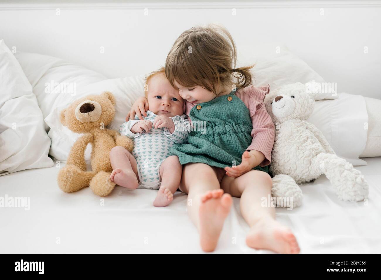 Frères et sœurs (2-5 mois, 2-3) assis au lit avec des ours en peluche Banque D'Images