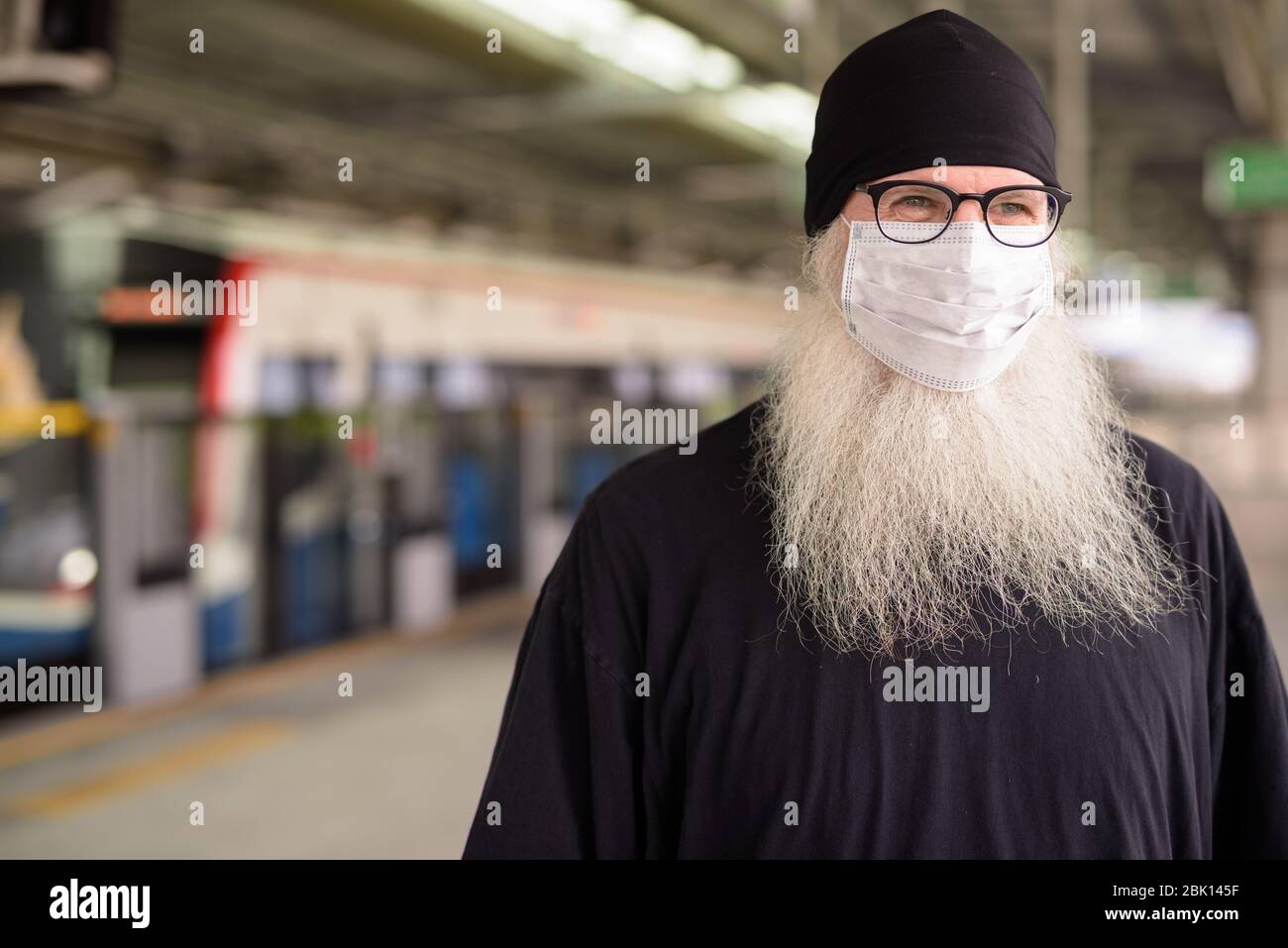 Visage d'un homme d'hipster mûr et barbu pensant avec masque pour la  protection contre l'éclosion du virus corona à la gare Photo Stock - Alamy
