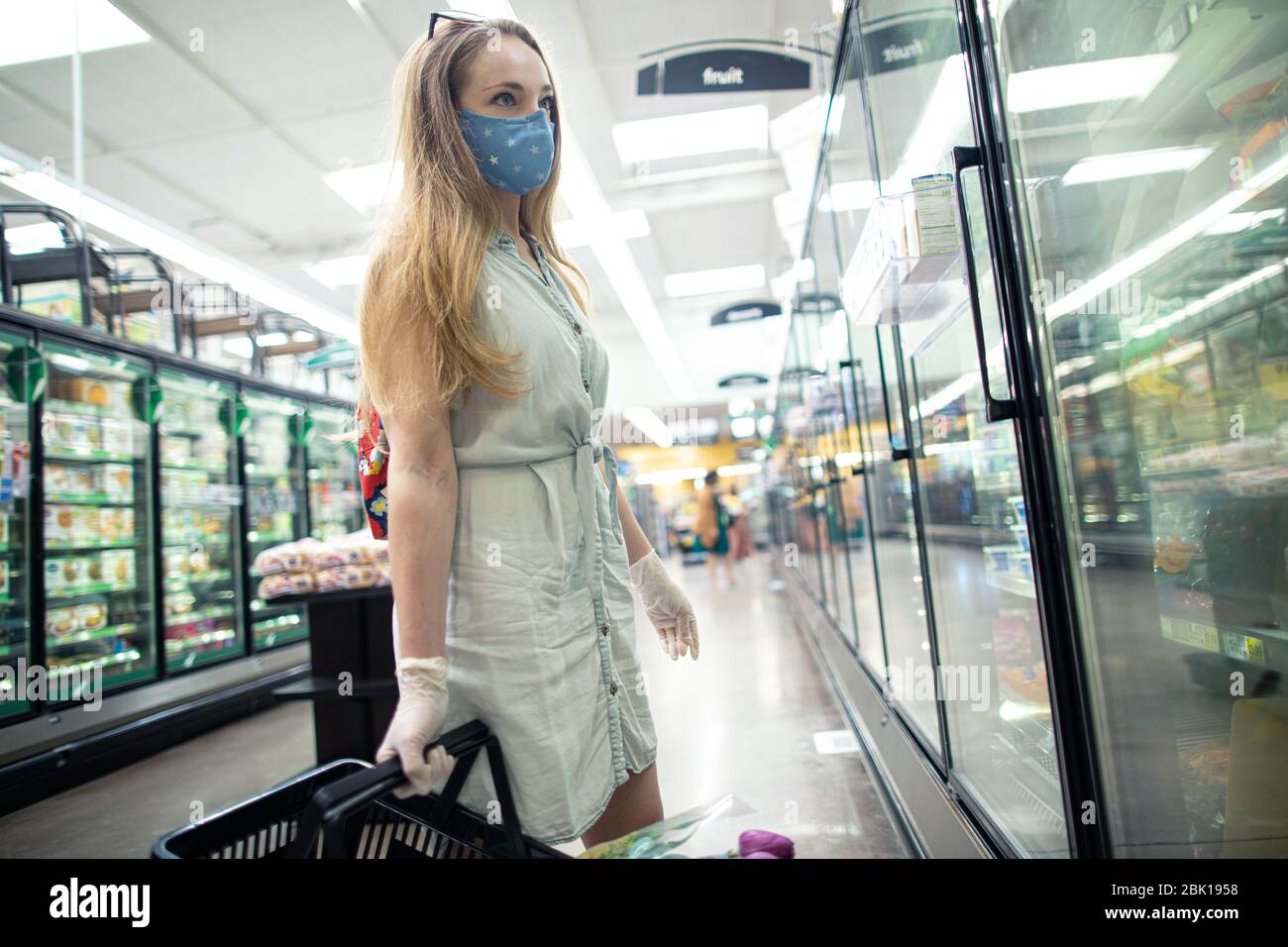 Une jeune femme d'une épicerie porte un masque facial et des gants jetables. Les personnes portant des masques en tissu se protègent contre la pandémie de covid-19. Banque D'Images