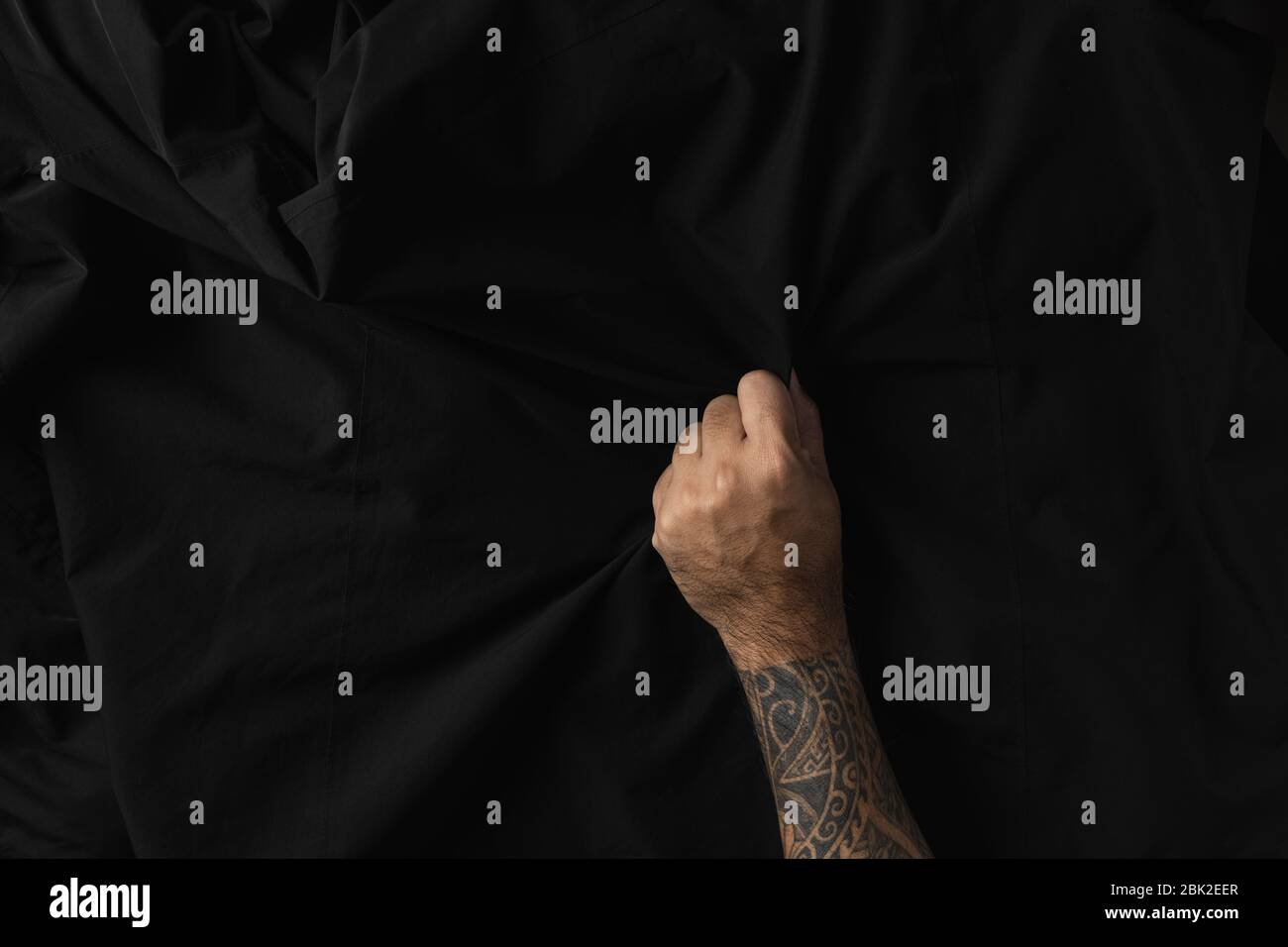 Homme main avec tatouages tenant la texture de tissu noir ridé. Banque D'Images