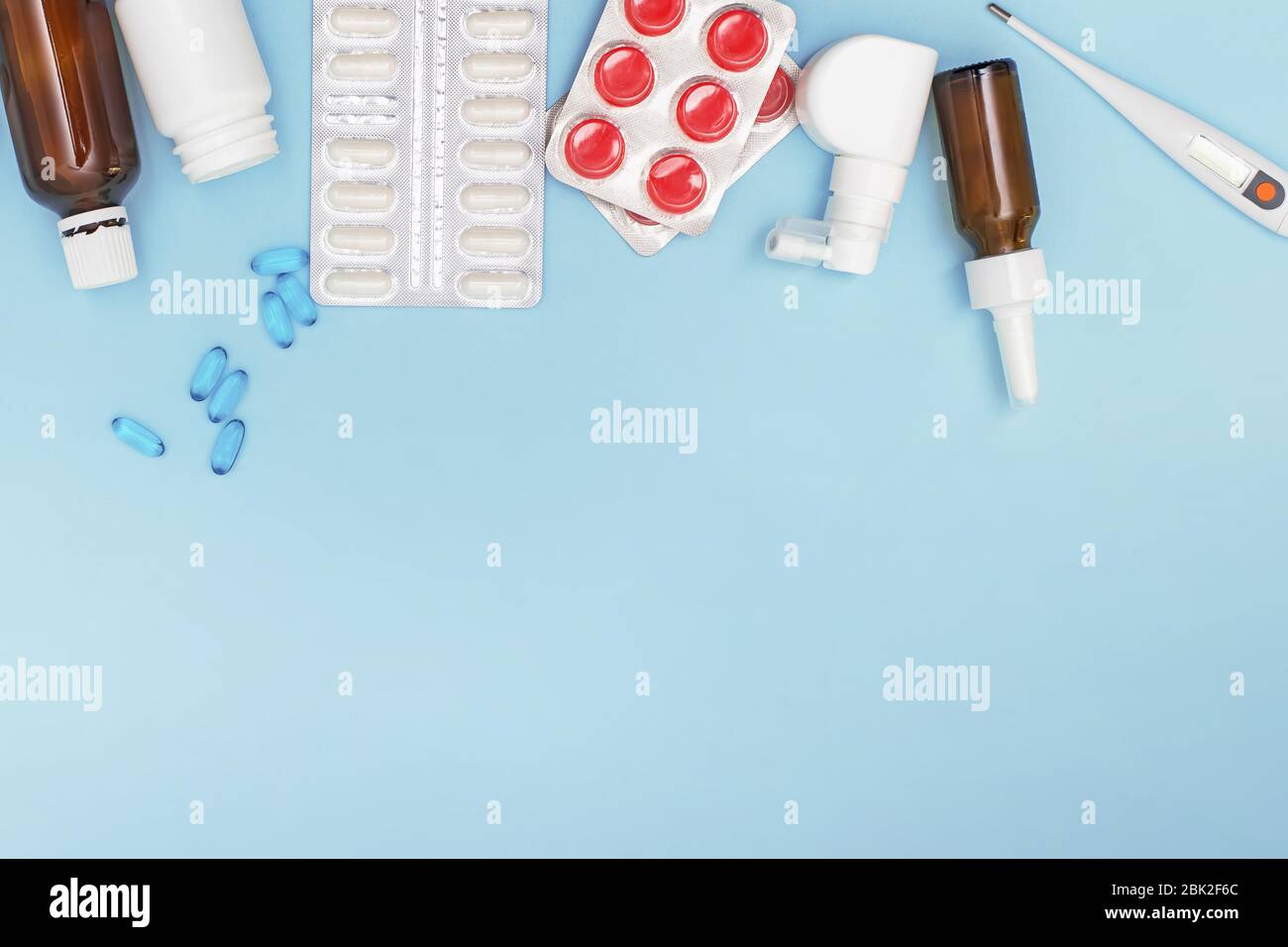Divers médicaments, un thermomètre, pulvérise un nez bouché et une douleur dans la gorge sur fond bleu. Banque D'Images