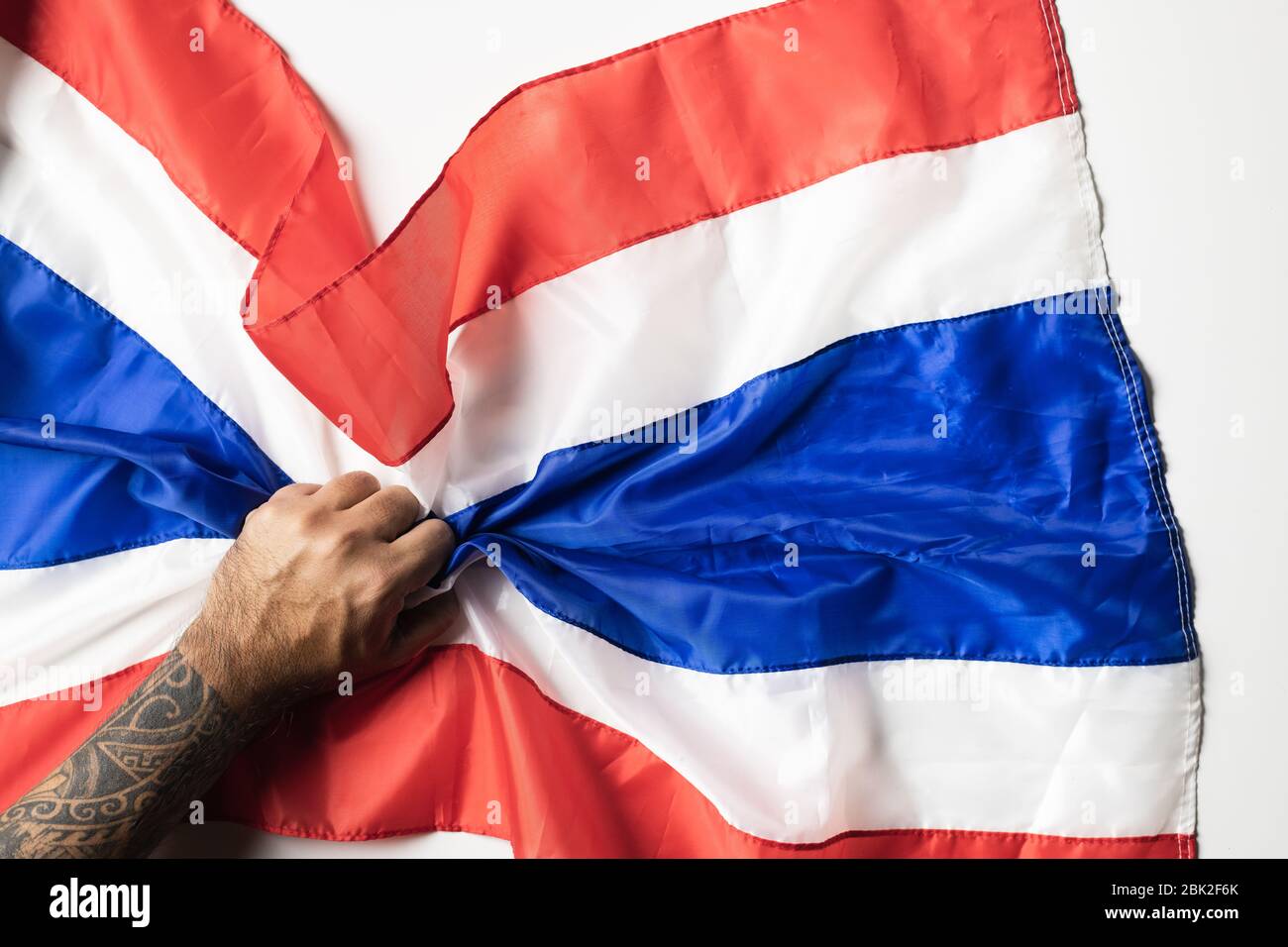 Main d'homme avec tatouages tenant drapeau de Thaïlande froissé sur fond blanc pour l'espace de copie. Banque D'Images
