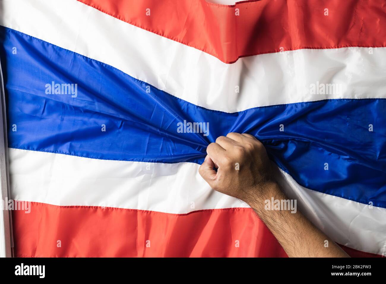 Main d'homme avec tatouages tenant drapeau de Thaïlande froissé sur fond blanc pour l'espace de copie. Banque D'Images
