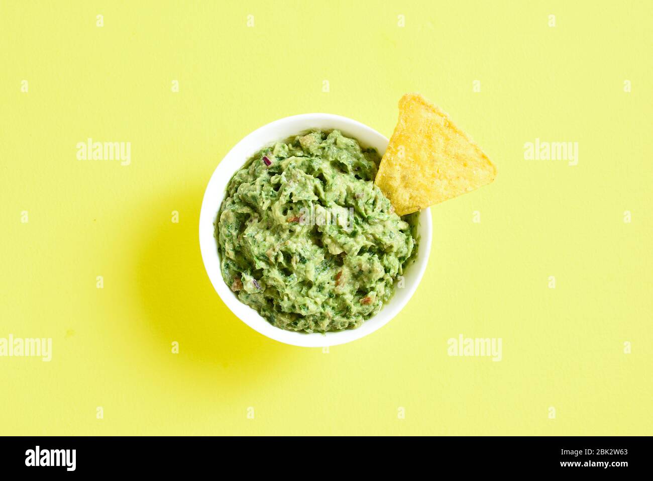 Guacamole tremper dans un bol sur fond jaune avec de l'espace texte libre. Propagation d'avocat en bonne santé. Vue sur le dessus, plat Banque D'Images