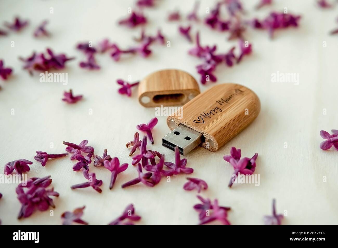 Clé USB marron en bois avec texte Happy moments avec pétales lilas sur fond en bois clair, stockage de données, beau téléchargement de photos au client Banque D'Images