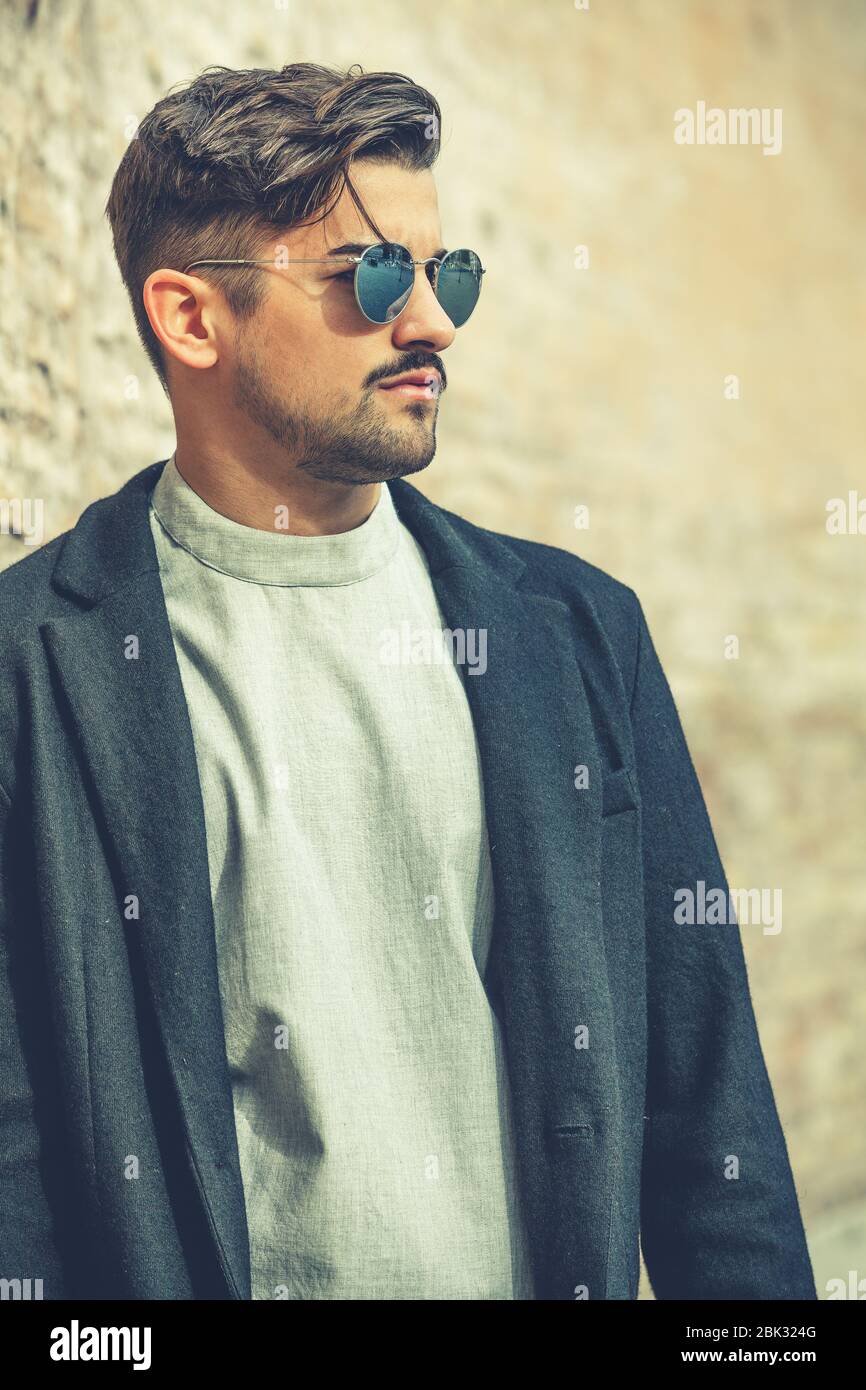 Bel homme élégant avec lunettes de soleil et coiffure moderne et barbe.  Extérieur dans la rue. T-shirt blanc et veste noire Photo Stock - Alamy