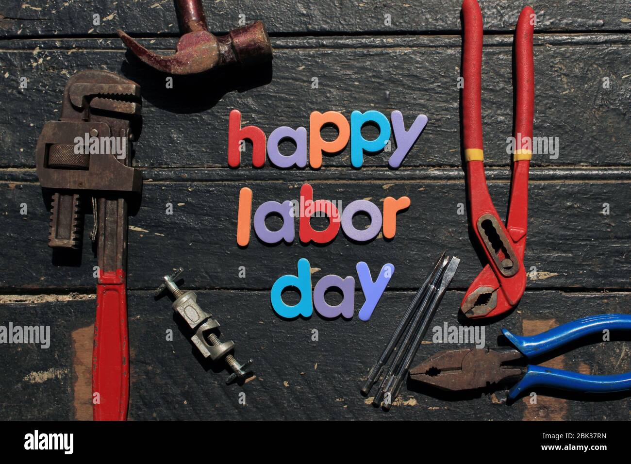 Texte Happy Labor Day en plusieurs couleurs sur fond de bois avec outils de réparation de construction. Signe de concept de la journée de travail. Banque D'Images