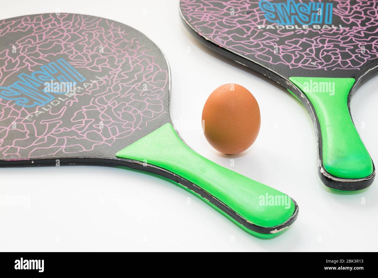 Un œuf repose et remplace la balle au milieu entre deux raquettes de tennis  de plage sur fond blanc, la composition exprime le concept de Photo Stock -  Alamy
