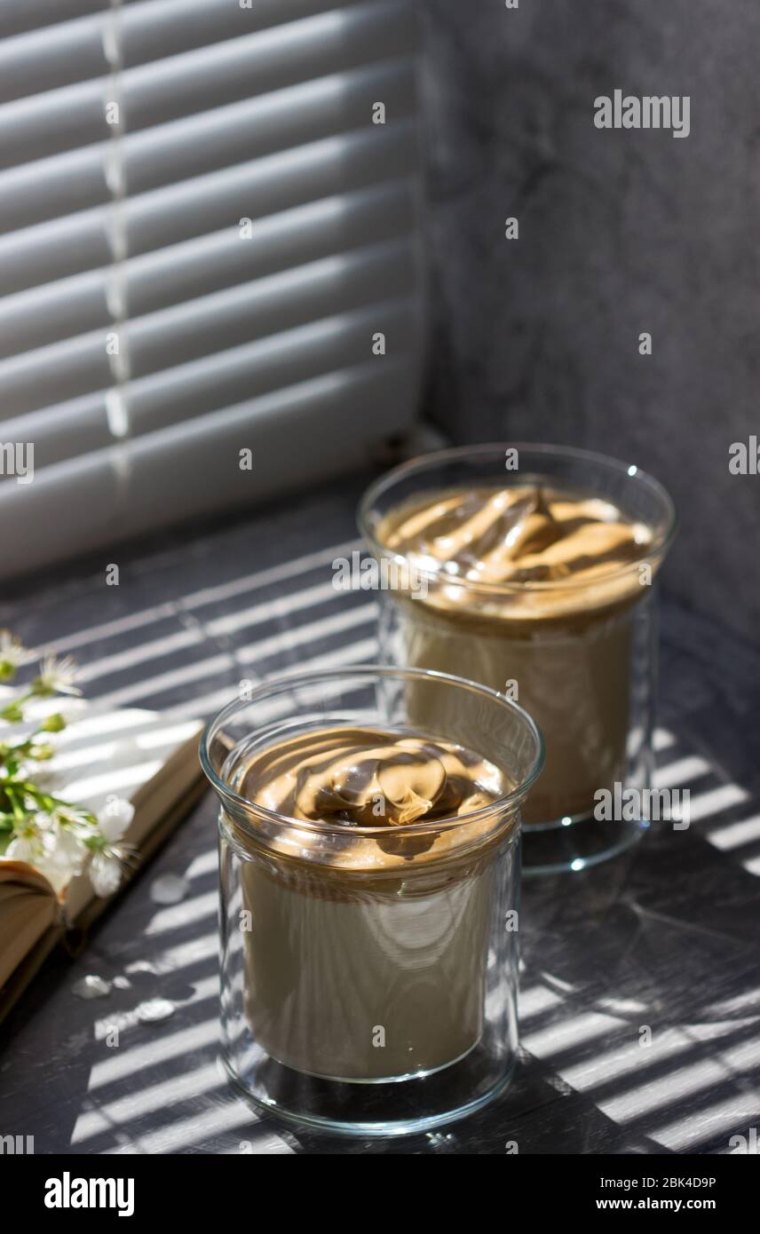 Dalgona café dans des verres transparents sur un seuil de fenêtre illuminé par la lumière du soleil. Banque D'Images