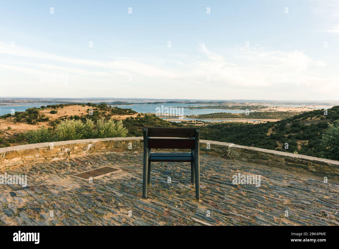Un magnifique point de vue du barrage d'Alqueva, avec une chaise en fer au premier plan, et les champs secs avec le blé typique et le corktree entourant le wat Banque D'Images