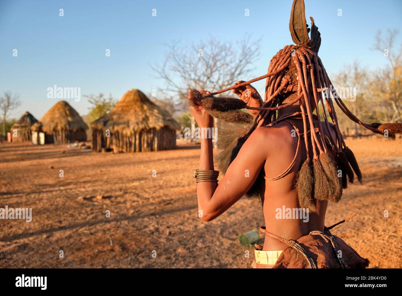 Batwa fille dans la robe traditionnelle combater ses cheveux au coucher du soleil. Banque D'Images