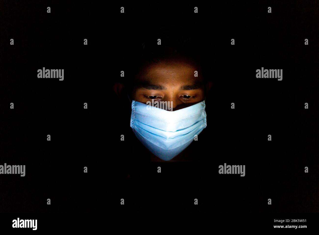 Un jeune homme bleu portant un masque chirurgical jouait à Dhaka pour jouer à des jeux sur smartphone. Banque D'Images