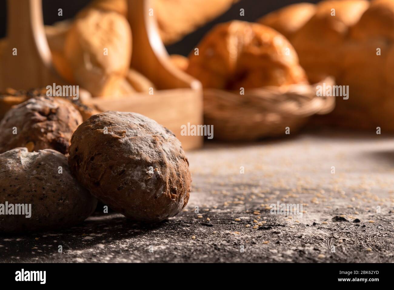 Des pains à la lumière du soleil se ferment le matin sur la table noire en bois avec sésame et variété de boulangerie. Banque D'Images