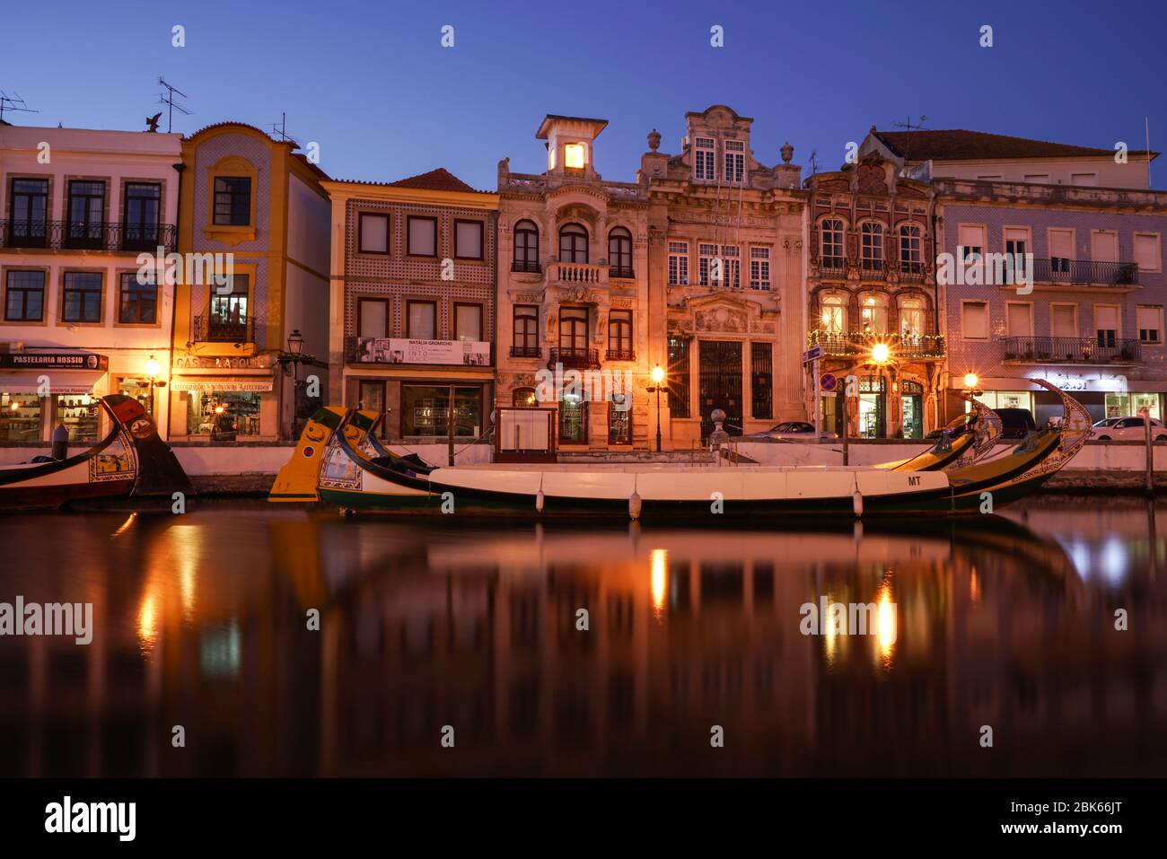 Aveiro, Portugal - avril 2019 : longue exposition des bateaux Moliceiro dans le canal de l'eau avec des bâtiments Art nouveau, après le coucher du soleil. Banque D'Images