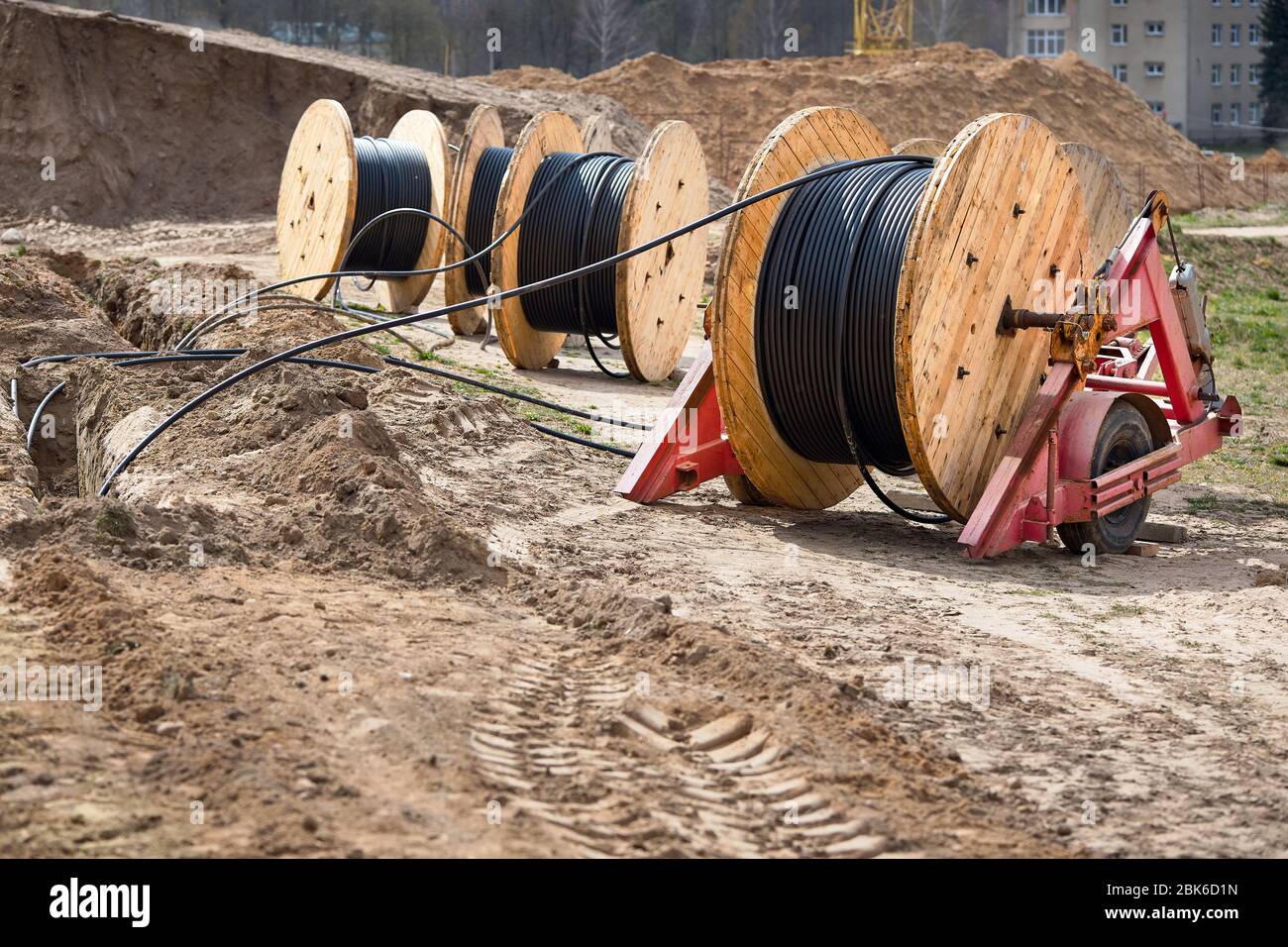 Plusieurs bobines de bois avec câble d'alimentation posé dans une tranchée. Concept de fourniture d'électricité pour les projets de construction. Banque D'Images