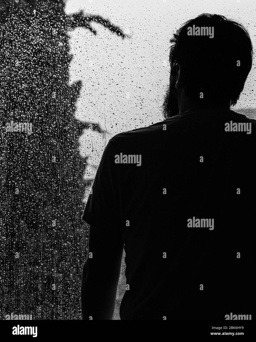 L'homme regarde la pluie à travers une fenêtre, pendant l'auto-isolation Banque D'Images