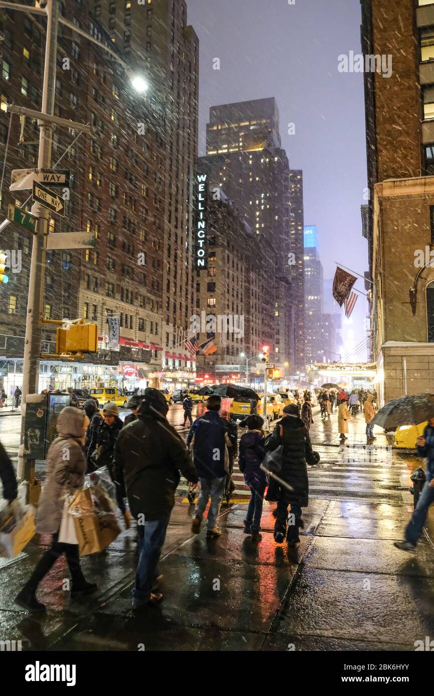 New York, NY/USA-décembre 2017 : coin de la 7ème Avenue et de la 56ème rue W la nuit. Des foules de touristes et de gens du coin passent devant lors d'une tempête de neige Banque D'Images