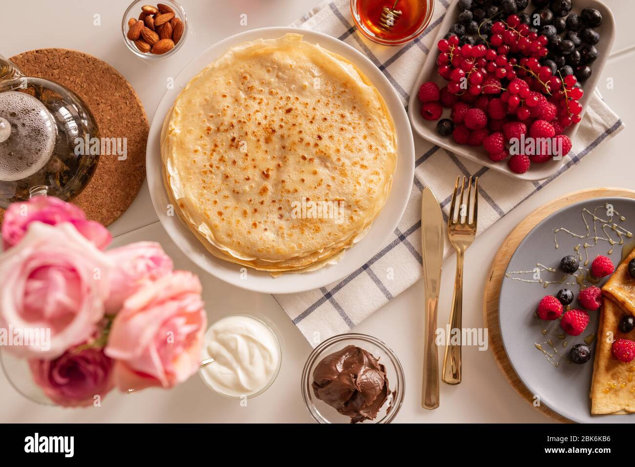 Plan plat de la table de cuisine servi pour le petit déjeuner - crêpes appétissantes, baies fraîches, tartiner au chocolat, crème au miel, amandes et thé Banque D'Images